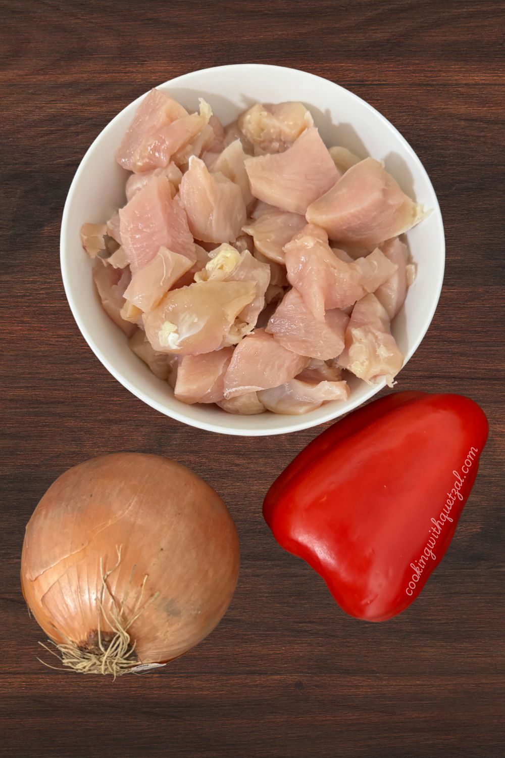 This image is of the ingredients needed for chicken fajitas. Cubed chicken, 1/2 an onion and colorful bell peppers.