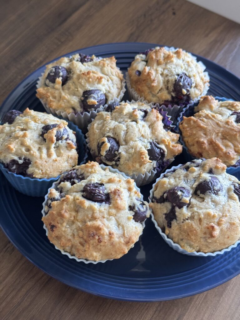 This image is of gluten free blueberry muffins arranged on a navy blue plate with a wood grain background.